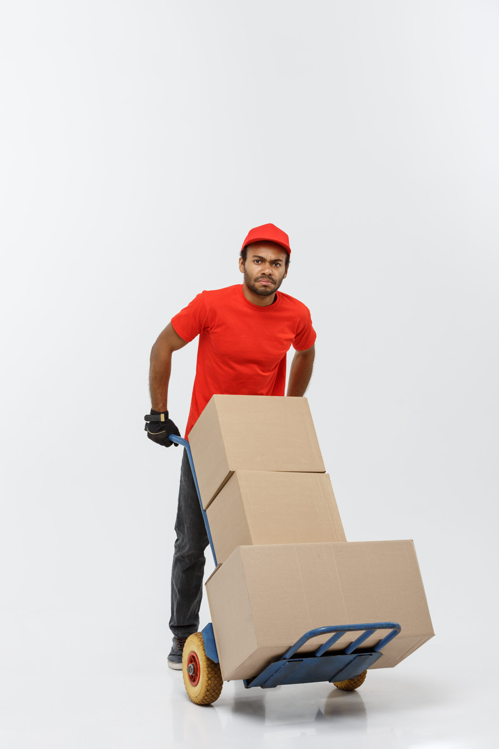 Delivery Concept - Portrait of Handsome African American delivery man or courier pushing hand truck with stack of boxes. Isolated on Grey studio Background. Copy Space. Delivery Concept - Portrait of Handsome African American delivery man or courier pushing hand truck with stack of boxes. Isolated on Grey studio Background. Copy Space.