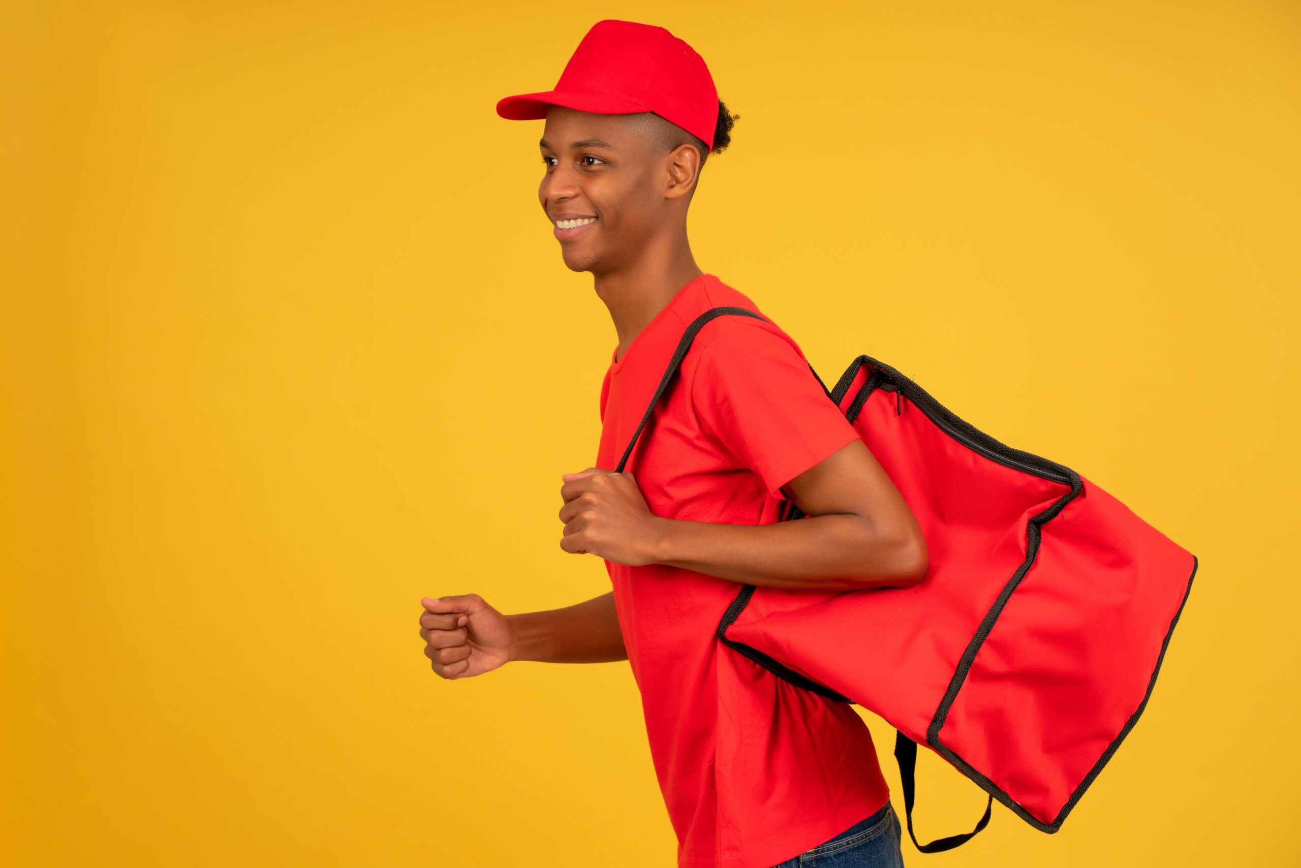 Young delivery man in red uniform running over isolated background. Portrait of young delivery man dressed in a red uniform running over isolated background. Delivery concept.